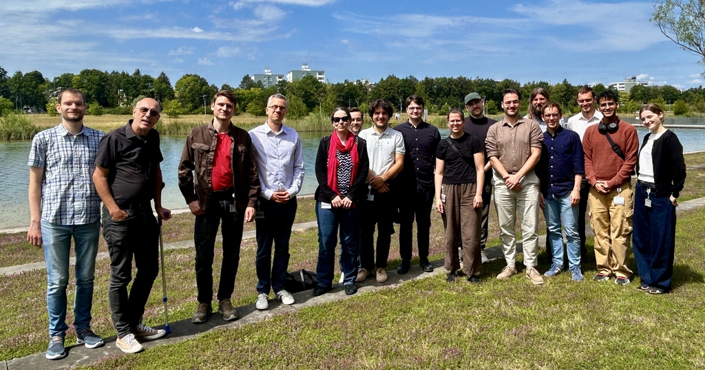 Gruppenfoto einer diversen Gruppe von Menschen im Freien vor einer Parklandschaft.
