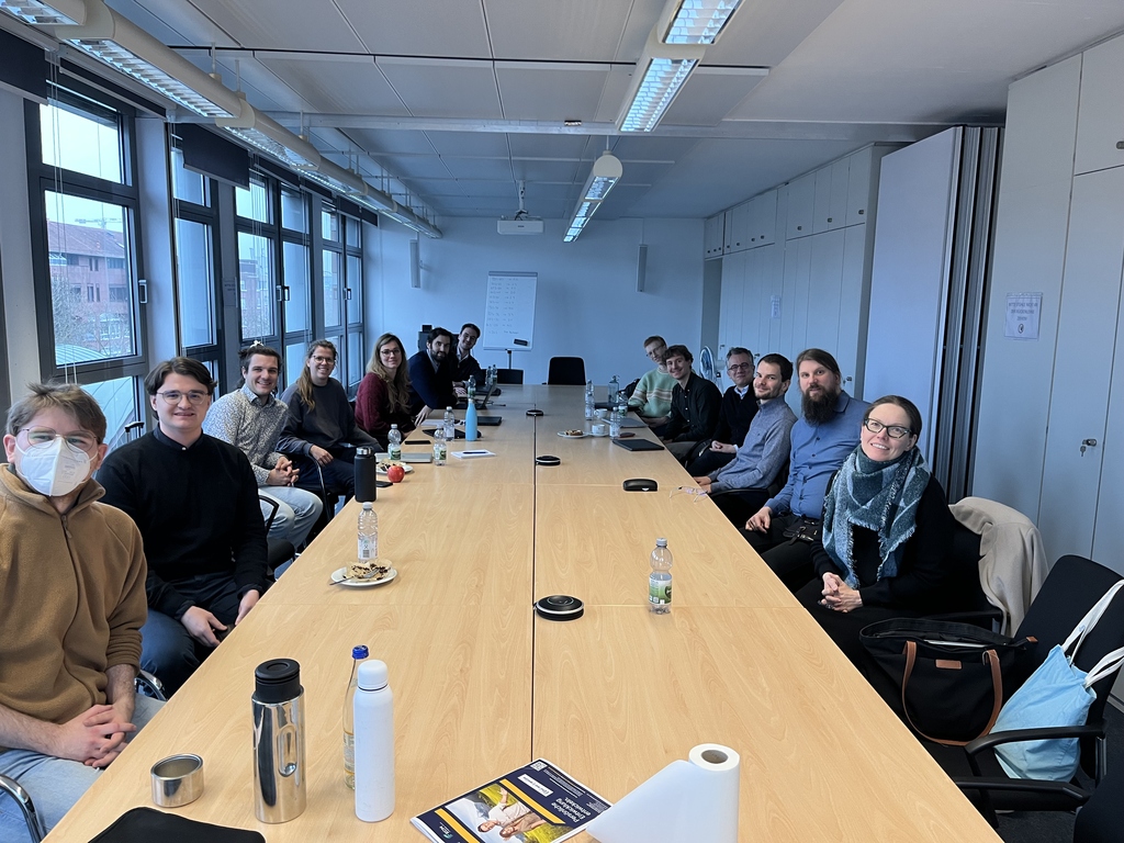 Gruppe von Menschen sitzt um einen langen Konferenztisch in einem Büroraum.